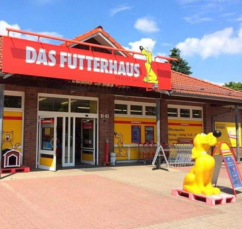 Chien publicitaire FUTTERHAUS 2 Sklep Das Futterhaus z czerwonym szyldem nad wejściem, żółtą figurką psa i plakatami.