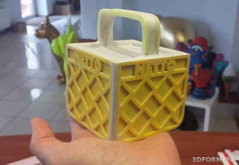 LOGO 3D NETTO 4 Mały model żółtej skrzynki z napisem "NETTO", trzymany na dłoni.