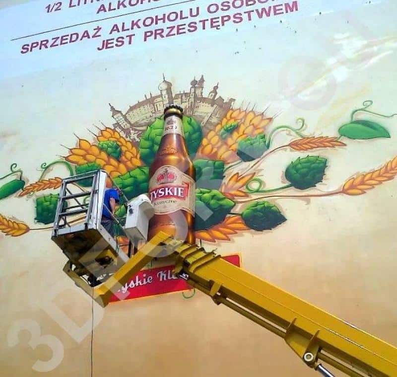 Fresque tridimensionnelle TYSKIE 2 Osoba na podnośniku malująca reklamę piwa Tyskie na ścianie budynku.