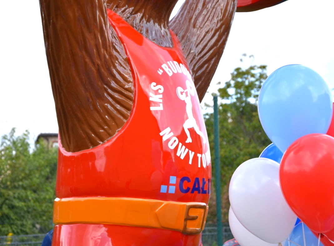 Grand Ours - Championnats d'Haltérophilie 1 Posąg niedźwiedzia w czerwonym stroju sportowym z białym napisem "LKS 'Budowlani' Nowy Tomyśl", w tle kolorowe balony.