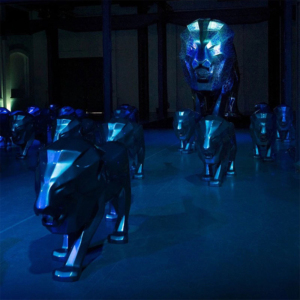 Sculptures de lions métalliques éclairées en bleu, placées dans une pièce sombre.
