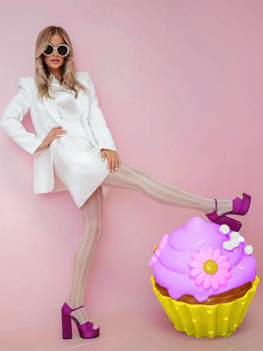 Un cupcake coloré pour la pâtisserie Sweet Home à Lagos, au Portugal 4 Kobieta w białym stroju, okularach przeciwsłonecznych i fioletowych butach na wysokim obcasie na tle różowej ściany, z fioletowo-żółtą dekoracyjną babeczką.