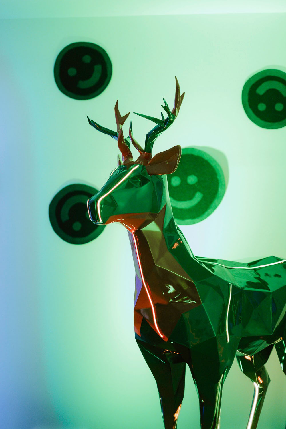 Cerfs Jägermeister avec Éclairage LED 7 Metaliczna rzeźba renifera na tle świecących, zielonych emoji.