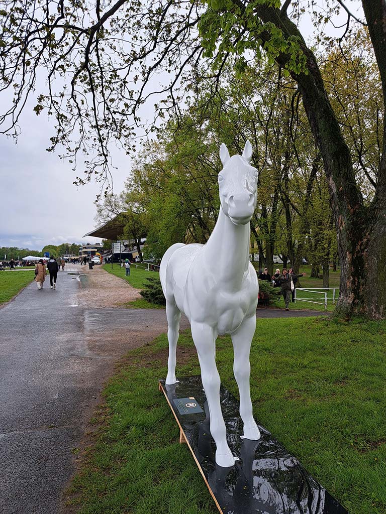 Les sculptures colorées de chevaux sur la piste de Partynice à Varsovie 3 Biała rzeźba konia stojąca na trawniku w parku.