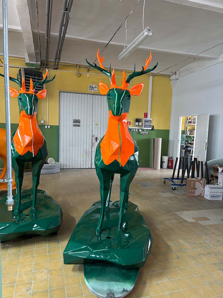 Cerfs Jägermeister avec Éclairage LED 6 Rzeźby jeleni wykonane z pomarańczowego i zielonego metalu w warsztacie.